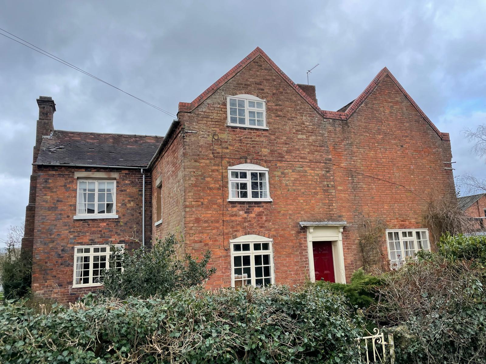Twin-gabled red-brick farmhouse front elevation with red door before renovation, Penkridge