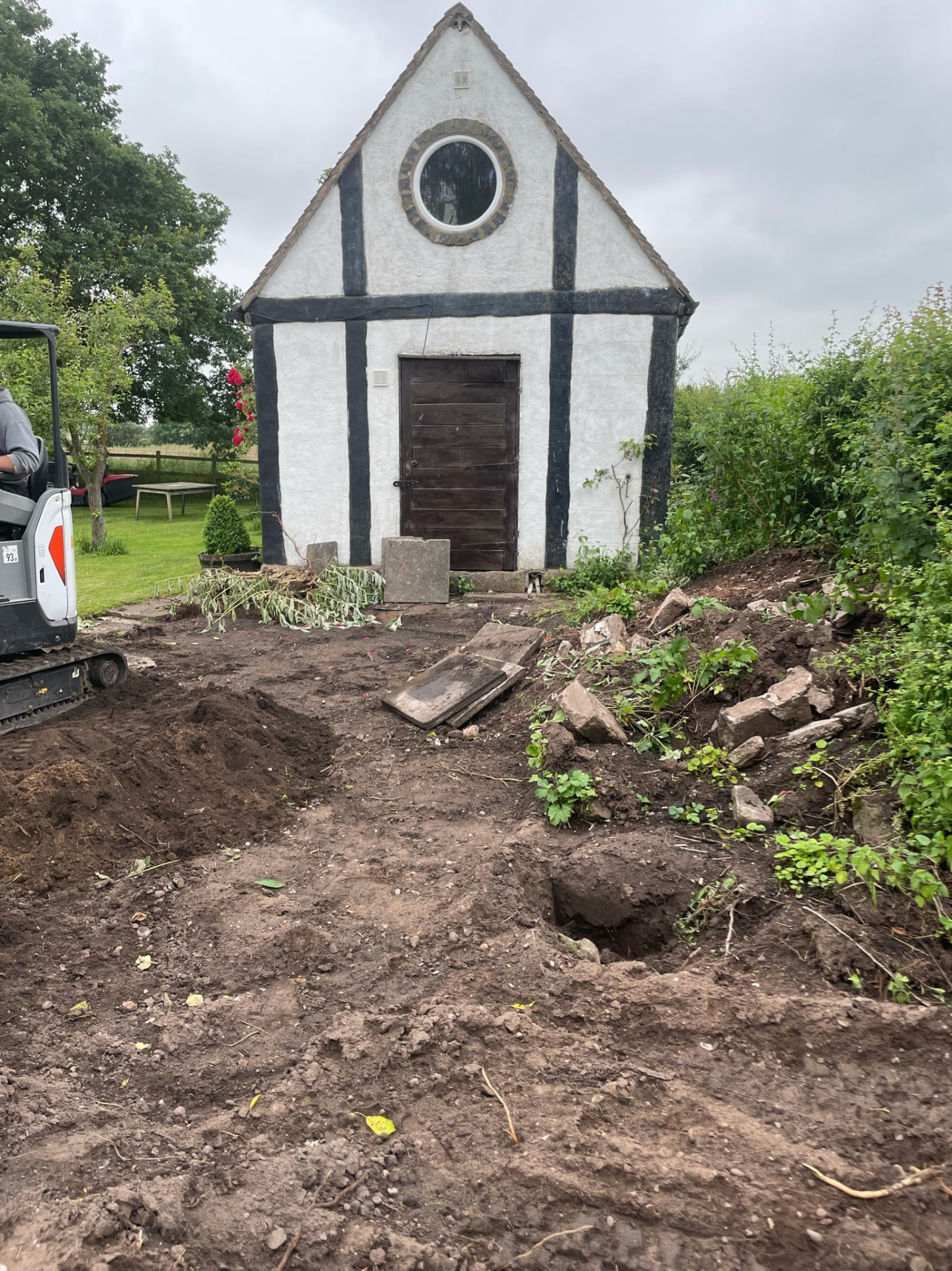 Mini digger carrying out groundworks beside a summer house before a new patio in Penkridge
